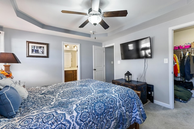 carpeted bedroom with ceiling fan, a walk in closet, a tray ceiling, and a closet