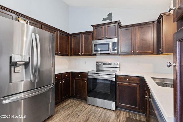 kitchen with wood-type flooring, appliances with stainless steel finishes, dark brown cabinets, and lofted ceiling