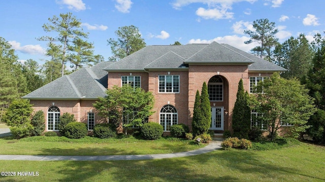 georgian-style home with brick siding, a shingled roof, a front yard, and french doors