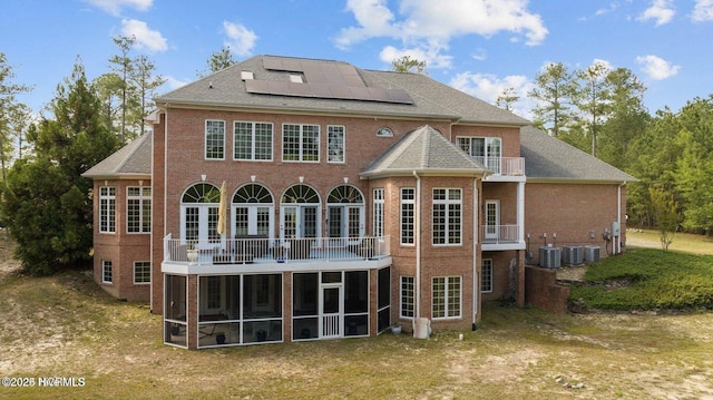 back of property featuring a balcony, a sunroom, roof mounted solar panels, and brick siding