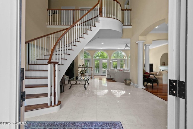 foyer entrance featuring arched walkways, a ceiling fan, a high ceiling, crown molding, and ornate columns