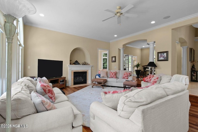 living room featuring arched walkways, ceiling fan, a fireplace with flush hearth, wood finished floors, and ornate columns