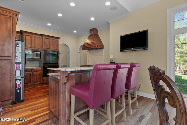 kitchen with stainless steel microwave, custom exhaust hood, a wealth of natural light, and dobule oven black