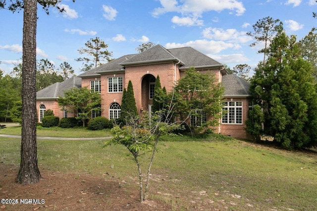 view of front of house featuring a front lawn, a shingled roof, and brick siding