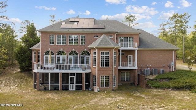 rear view of house featuring a balcony, central AC, brick siding, a sunroom, and roof mounted solar panels