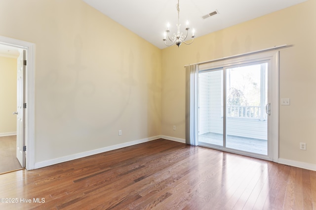 empty room featuring lofted ceiling, a notable chandelier, and hardwood / wood-style flooring