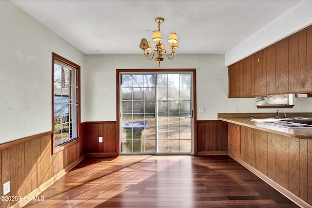 unfurnished dining area with wooden walls, dark hardwood / wood-style floors, and a notable chandelier