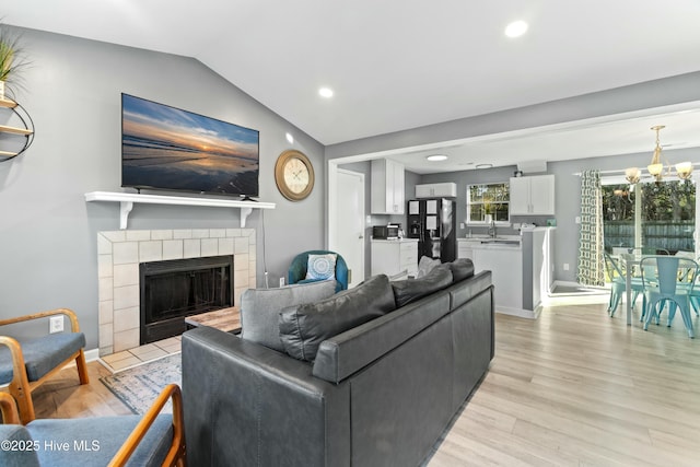 living room with vaulted ceiling, sink, a chandelier, a tiled fireplace, and light hardwood / wood-style flooring