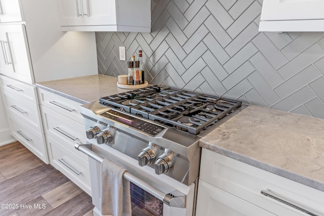 kitchen with white cabinetry, backsplash, light stone counters, stainless steel range, and light hardwood / wood-style floors