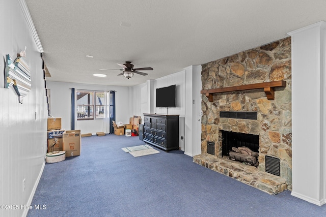 unfurnished living room with a stone fireplace, carpet flooring, ceiling fan, crown molding, and a textured ceiling