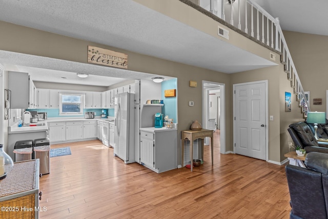 kitchen with sink, white appliances, white cabinetry, light hardwood / wood-style floors, and a textured ceiling