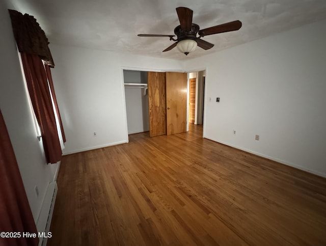 unfurnished bedroom featuring ceiling fan, wood-type flooring, a baseboard heating unit, and a closet