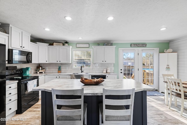 kitchen featuring sink, backsplash, a center island, black appliances, and white cabinets