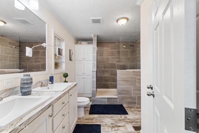 bathroom featuring vanity, toilet, a textured ceiling, and a tile shower