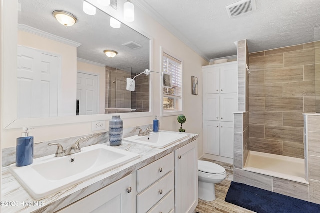 bathroom featuring ornamental molding, a tile shower, a textured ceiling, and toilet