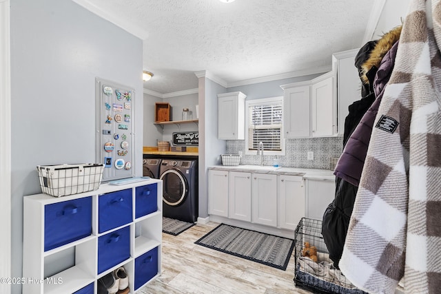 kitchen featuring sink, crown molding, white cabinetry, washing machine and dryer, and decorative backsplash