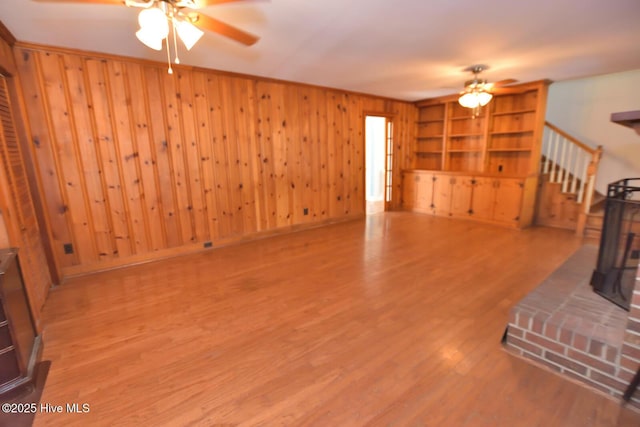 living room featuring built in features, hardwood / wood-style flooring, a wood stove, and ceiling fan