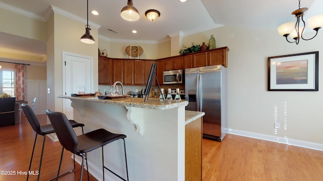 kitchen featuring a kitchen bar, light stone countertops, crown molding, pendant lighting, and stainless steel appliances