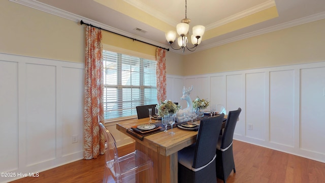 dining area with light wood-type flooring, a chandelier, crown molding, and a tray ceiling