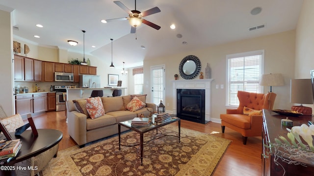 living room with ceiling fan, vaulted ceiling, and light wood-type flooring