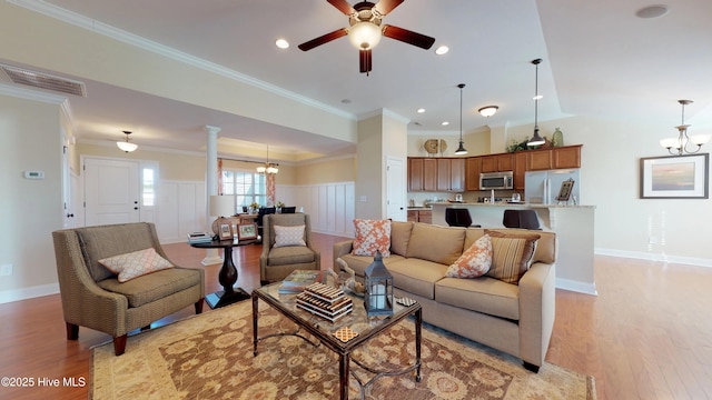 living room with decorative columns, light hardwood / wood-style flooring, ornamental molding, and ceiling fan with notable chandelier