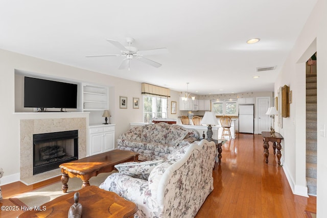 living room with ceiling fan with notable chandelier, a premium fireplace, light hardwood / wood-style floors, and built in features