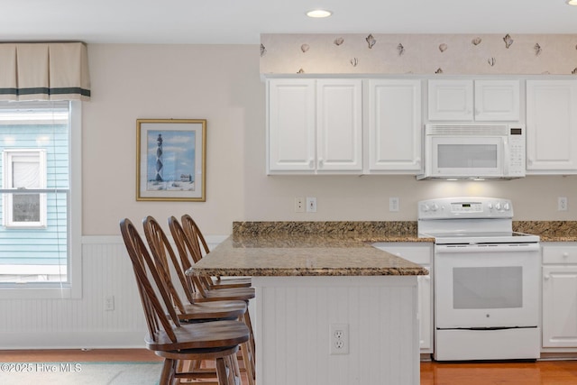 kitchen with white appliances, a breakfast bar, white cabinets, and stone counters