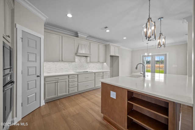 kitchen featuring sink, a kitchen island with sink, decorative light fixtures, and custom range hood