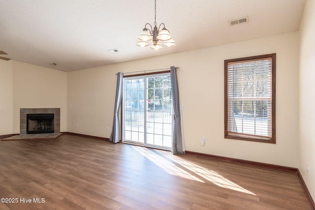 unfurnished living room with an inviting chandelier, hardwood / wood-style floors, a wealth of natural light, and a fireplace