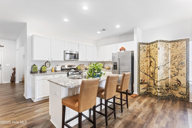 kitchen featuring light stone counters, a center island with sink, appliances with stainless steel finishes, a kitchen breakfast bar, and white cabinets