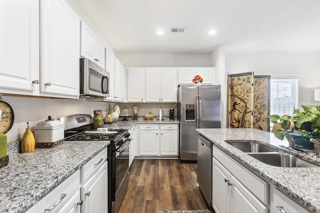 kitchen with sink, appliances with stainless steel finishes, white cabinetry, dark hardwood / wood-style floors, and light stone counters