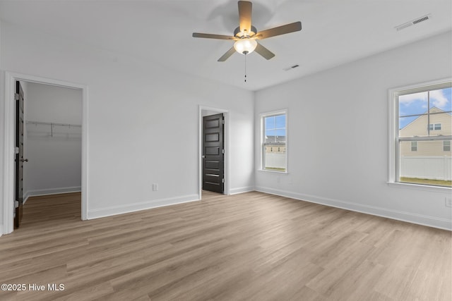 unfurnished bedroom featuring ceiling fan, a spacious closet, light hardwood / wood-style floors, and multiple windows