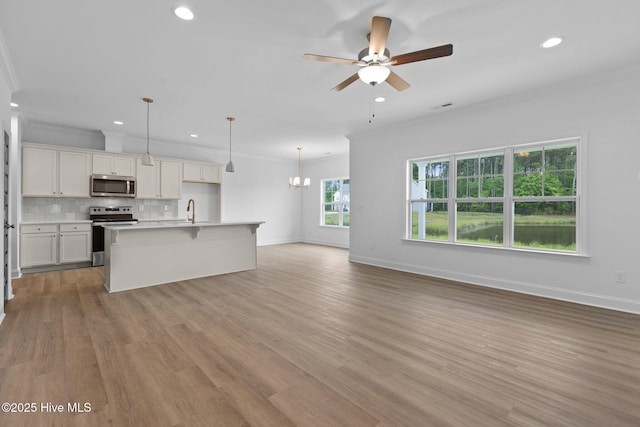 kitchen with appliances with stainless steel finishes, white cabinetry, sink, pendant lighting, and an island with sink