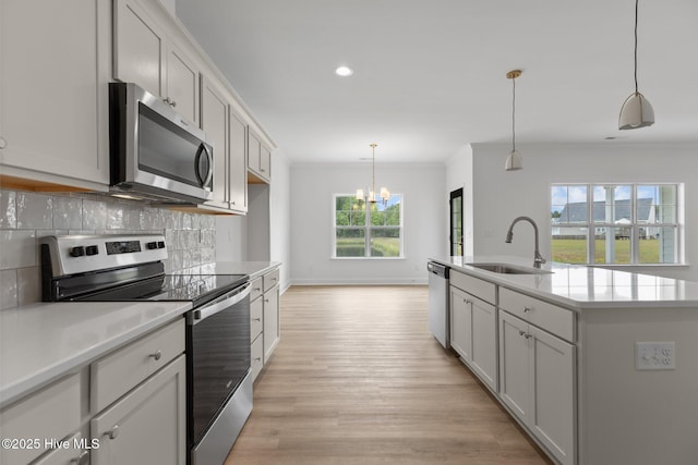 kitchen featuring pendant lighting, stainless steel appliances, an island with sink, decorative backsplash, and sink