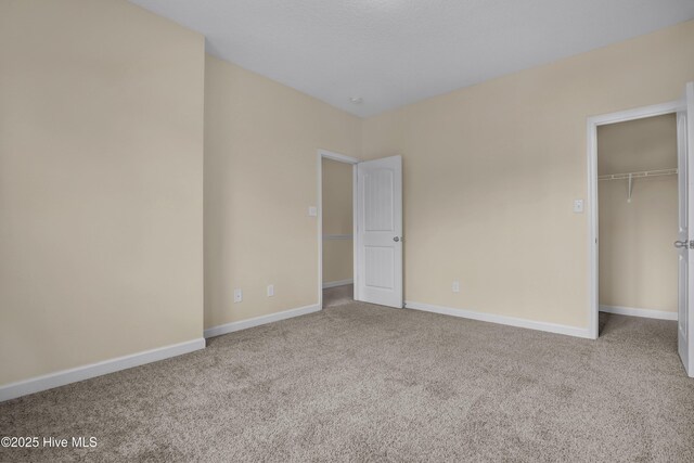 unfurnished bedroom with a walk in closet, a closet, a textured ceiling, and carpet flooring