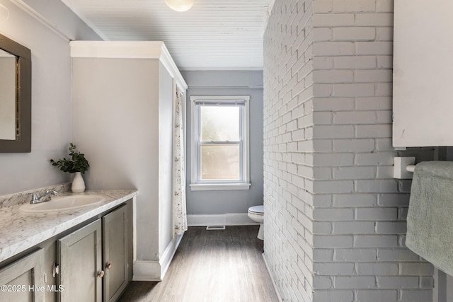 bathroom featuring vanity, brick wall, wood-type flooring, and toilet