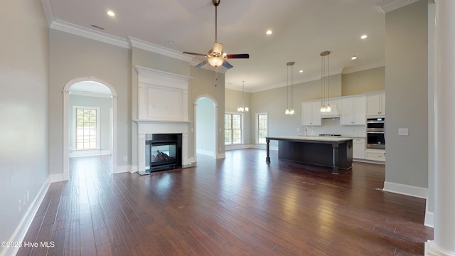 unfurnished living room with a multi sided fireplace, dark hardwood / wood-style floors, ceiling fan, and a healthy amount of sunlight