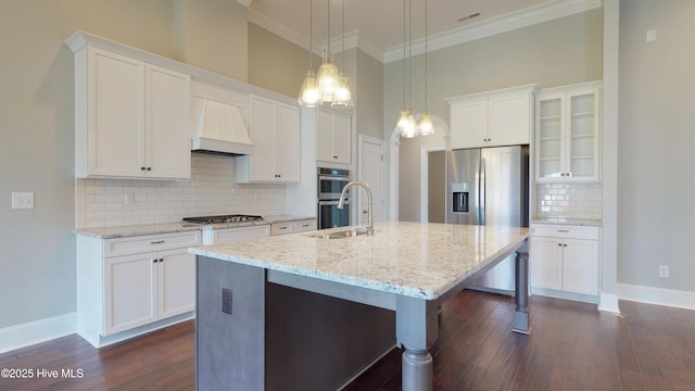 kitchen with appliances with stainless steel finishes, premium range hood, white cabinetry, a kitchen island with sink, and sink