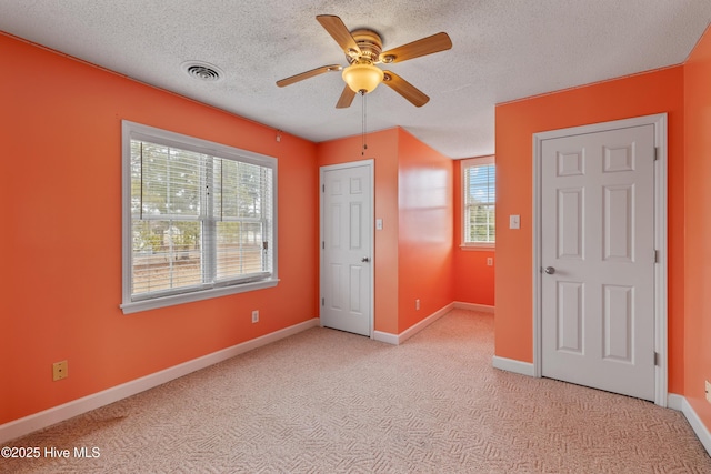 unfurnished bedroom featuring multiple windows, a textured ceiling, light colored carpet, and ceiling fan