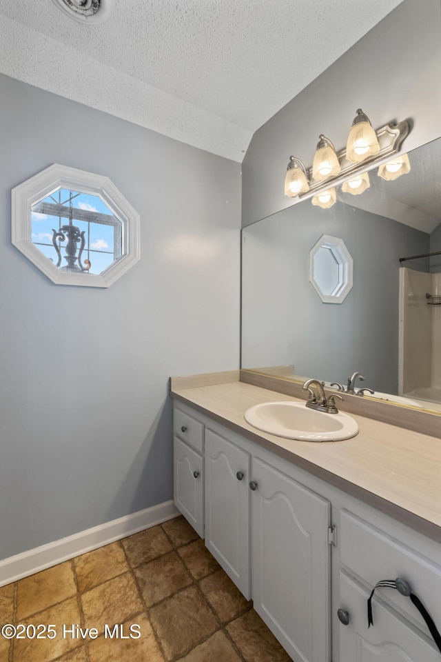 bathroom featuring vanity, vaulted ceiling, and a textured ceiling