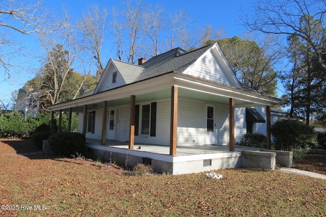 view of side of property with crawl space, covered porch, a chimney, and roof with shingles