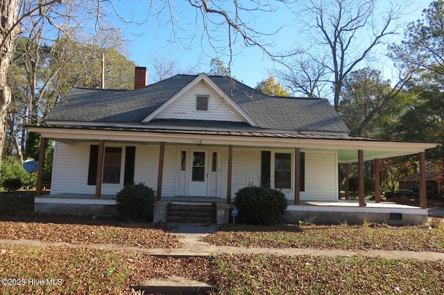 country-style home with covered porch, roof with shingles, and a chimney