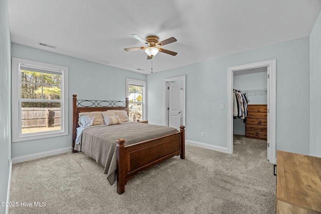 bedroom featuring a spacious closet, a closet, light carpet, and ceiling fan