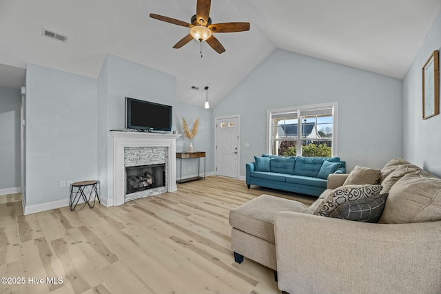 living room featuring ceiling fan, a stone fireplace, light hardwood / wood-style flooring, and high vaulted ceiling