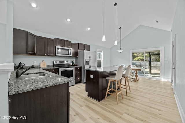 kitchen with hanging light fixtures, appliances with stainless steel finishes, sink, light stone counters, and a center island