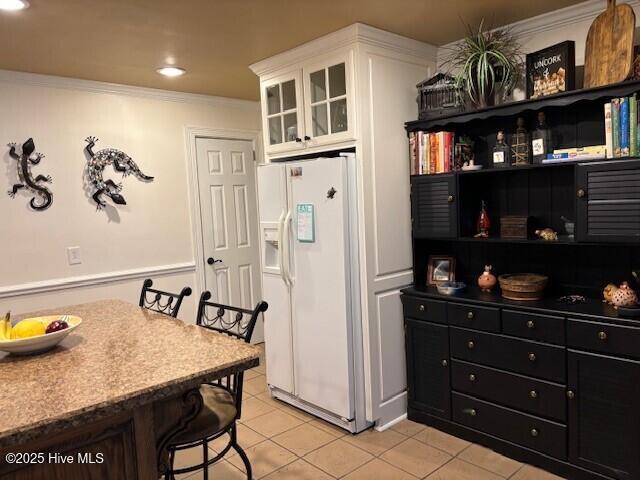 kitchen with white cabinetry, crown molding, light tile patterned floors, and white fridge with ice dispenser