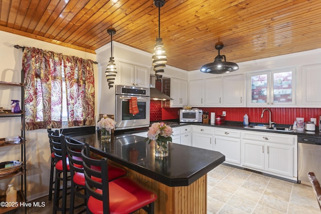 kitchen featuring appliances with stainless steel finishes, a kitchen bar, white cabinetry, sink, and hanging light fixtures