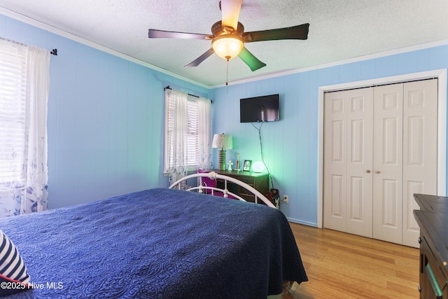 bedroom with a textured ceiling, a closet, light wood-type flooring, ornamental molding, and ceiling fan