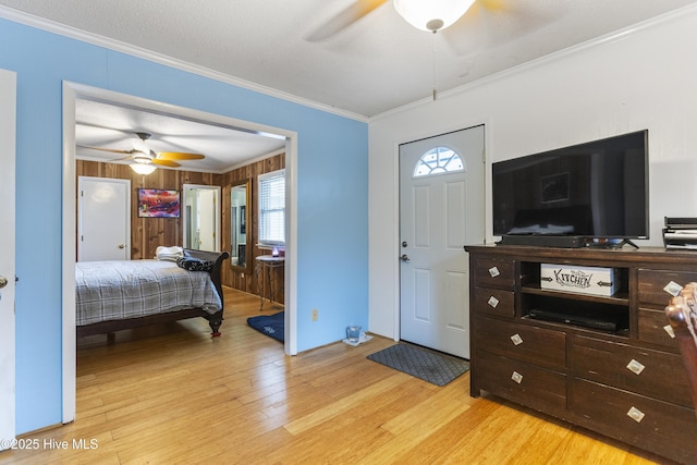 bedroom with ceiling fan, crown molding, light hardwood / wood-style flooring, and wood walls