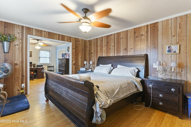 bedroom featuring light hardwood / wood-style flooring, ceiling fan, a textured ceiling, ornamental molding, and wood walls